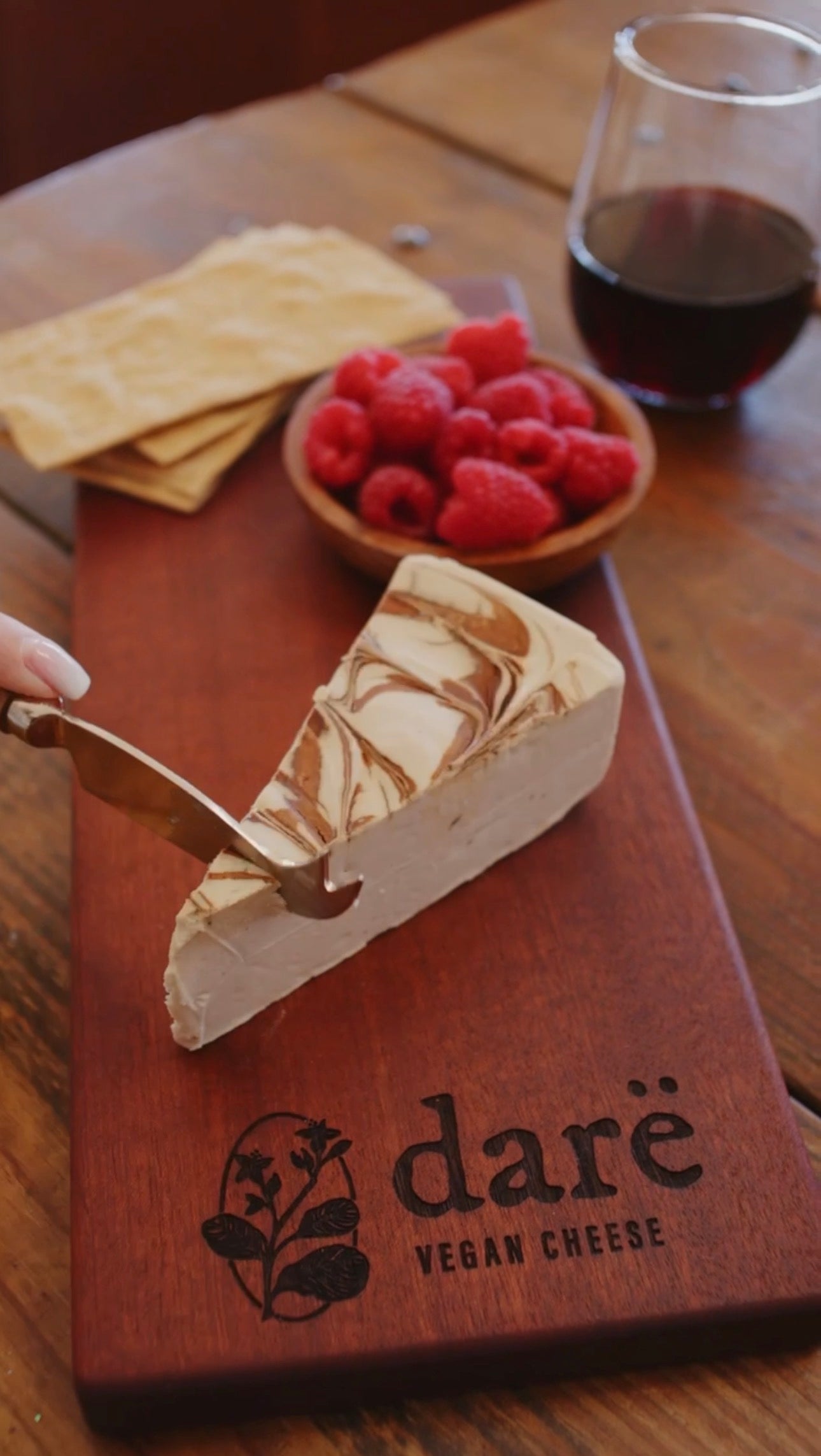 Cheese knife cutting to Dare Balsamic Fig on a wooden board and red wine in the background