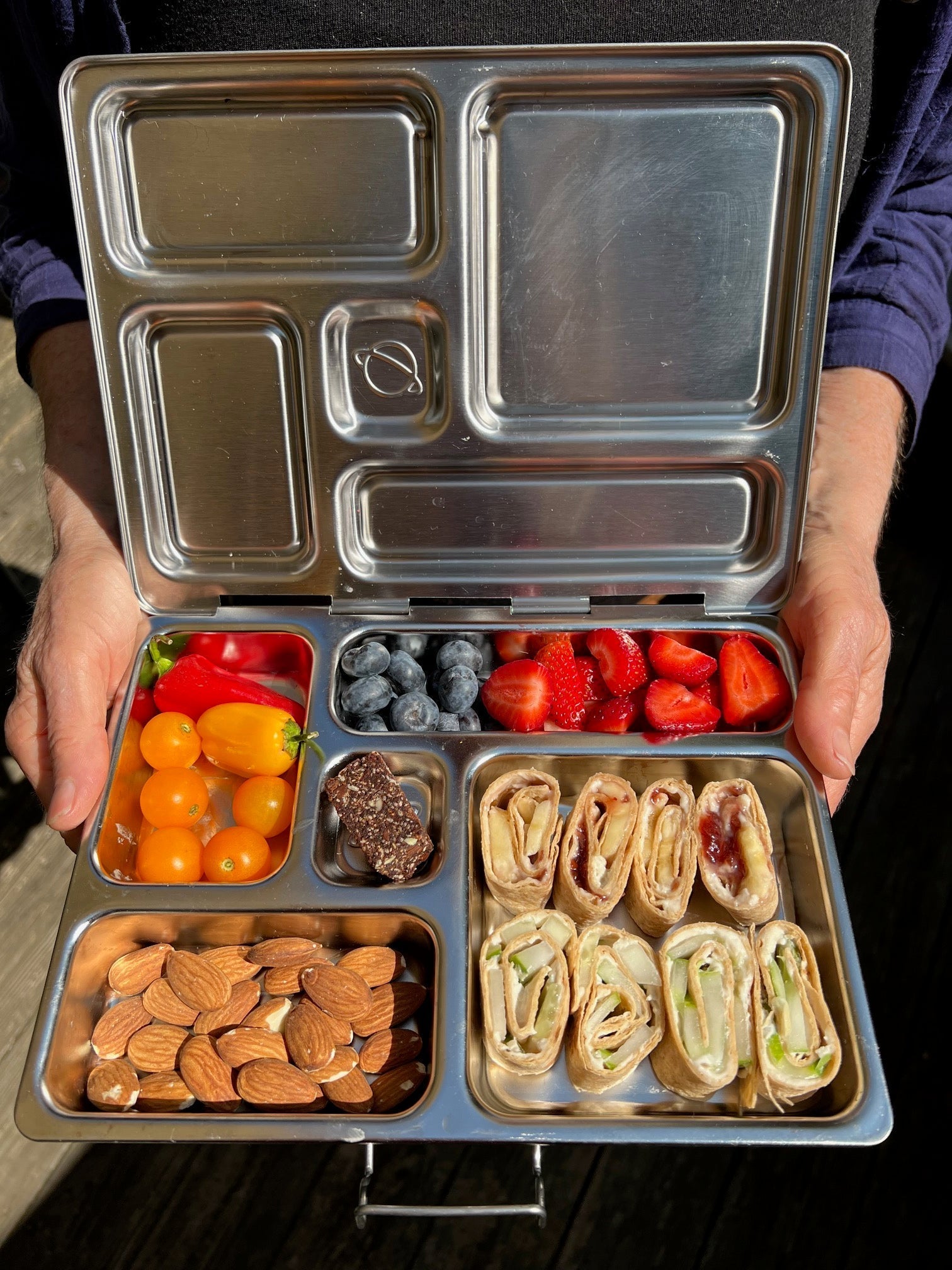 Vegan lunch box open showing pinwheels, veggies, fruit, nuts