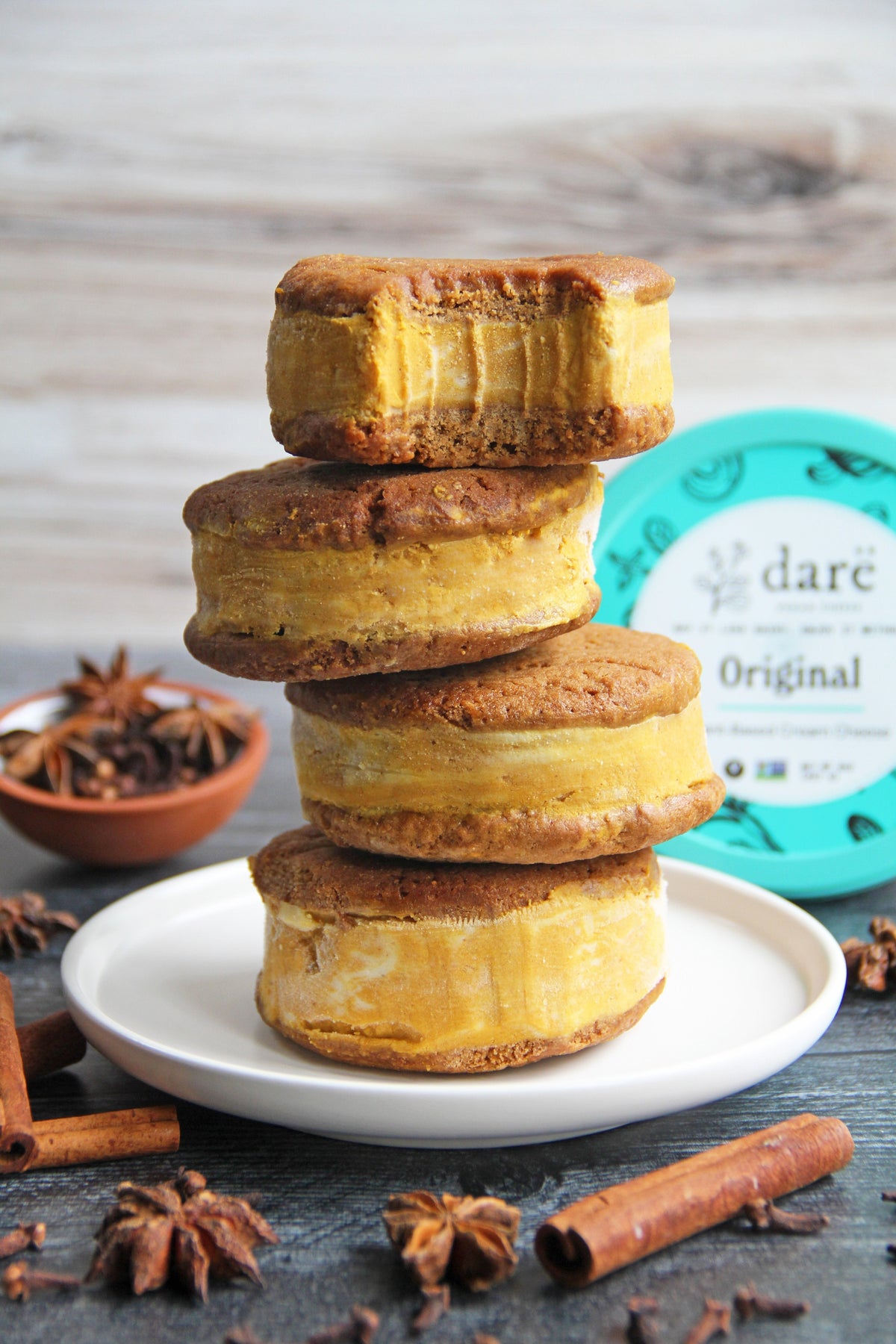 Golden pumkin ice cream sandwiches stacked on a white plate with Darë Original Cream Cheese packaging in background.