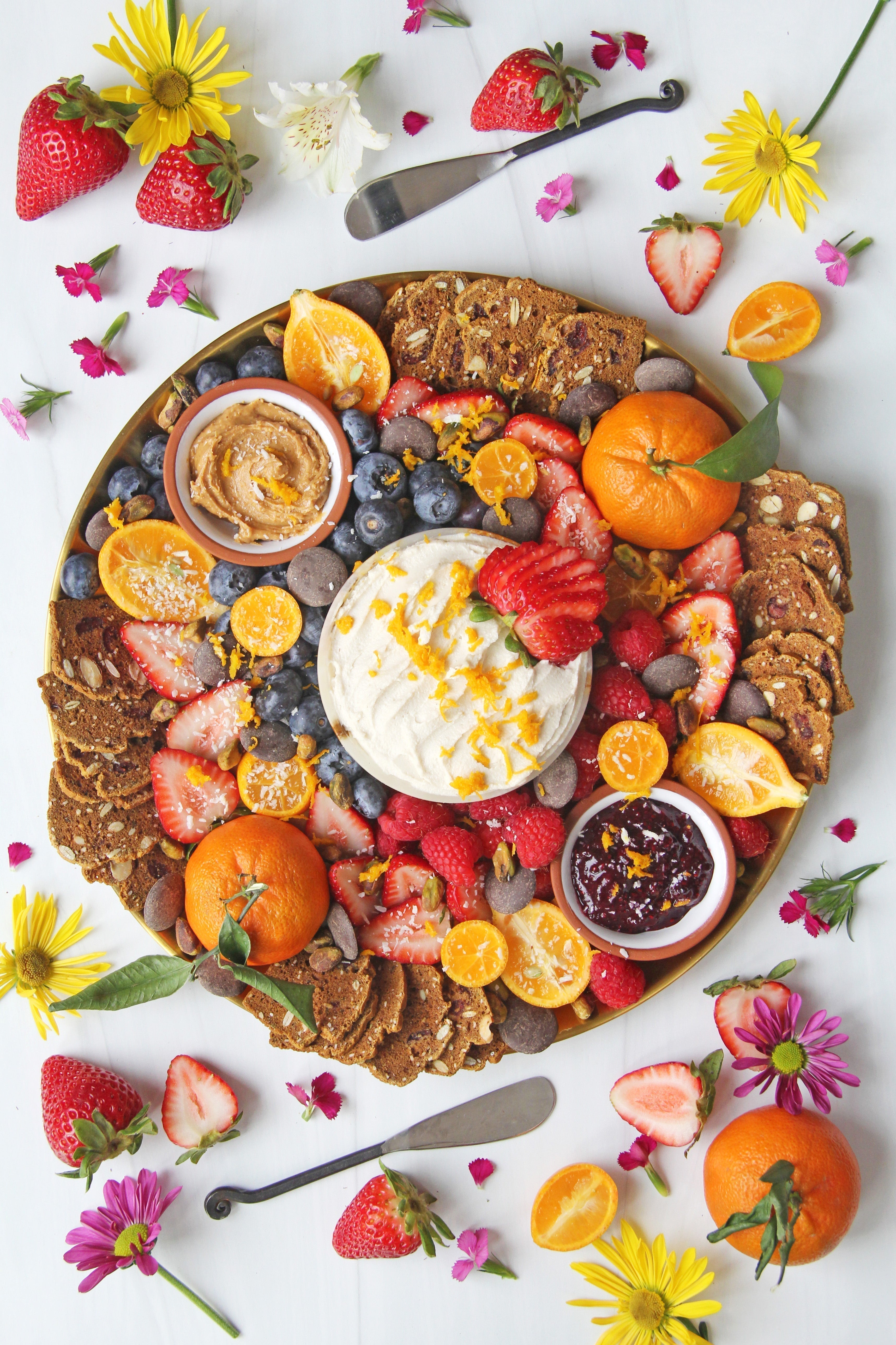 Colorful cheeseboard with fruits, chocolate and dairy free cheese surrounded by fruits and flowers