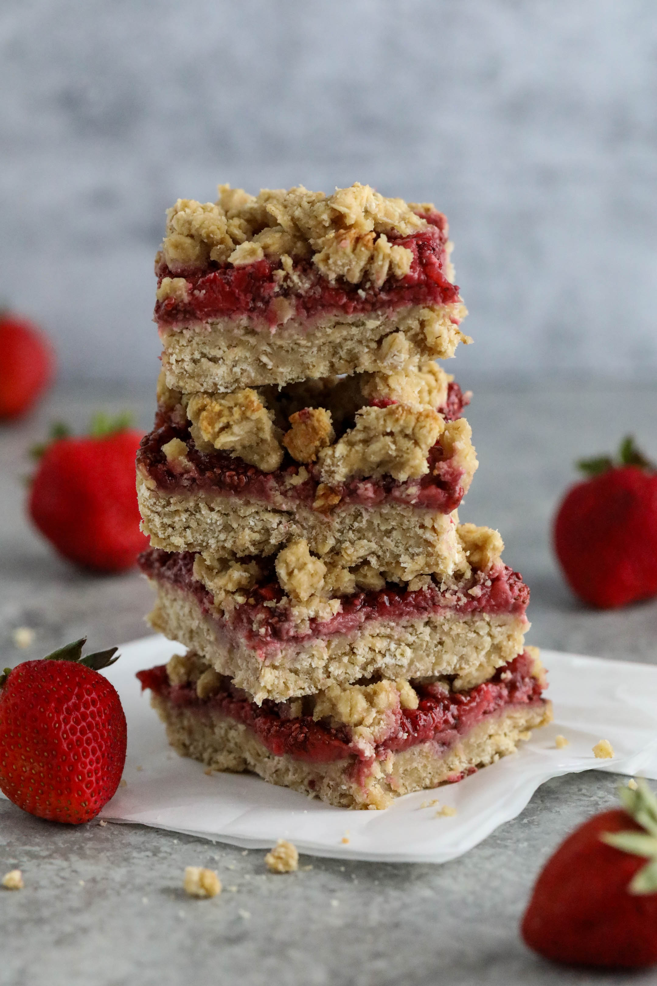 Stack of oatmeal bars atop a napkin surrounded by strawberries