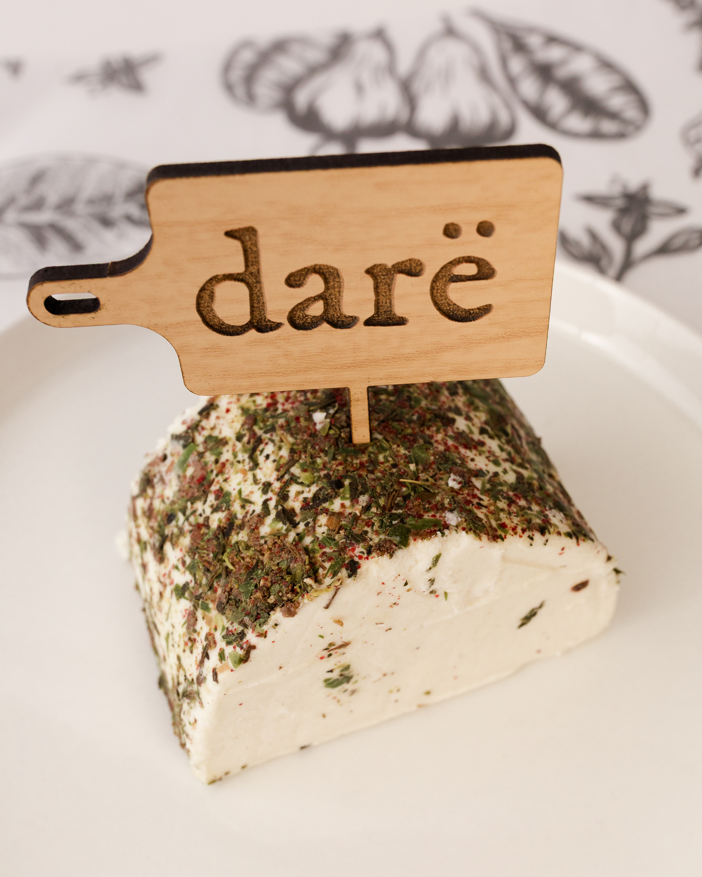 Block of cheese with a wooden sign labeled 'daré' on a white surface.