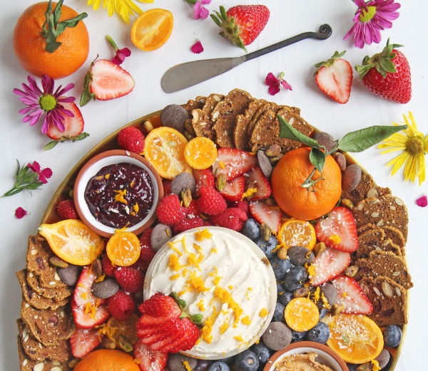 Assorted fruits, crackers, and a spread on a white surface with flowers.