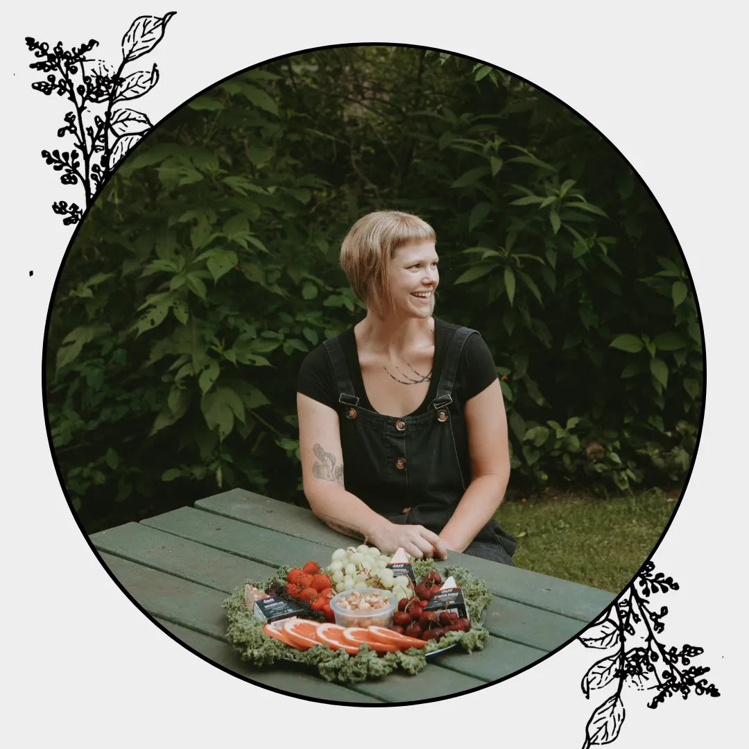 Gwendolyn Dare Hageman headshot, Founder of Darë Vegan Cheese, sitting at picnic bench in nature with vegan cheese platter