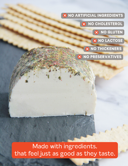 Load image 1 in gallery view. A close-up of a round of Dare Vegan Cheese goat cheese with a herb-dusted rind, placed on a dark slate board with crackers blurred in the background. Text overlays highlight product benefits: no artificial ingredients, no cholesterol, no gluten, no lactose, no thickeners, and no preservatives.