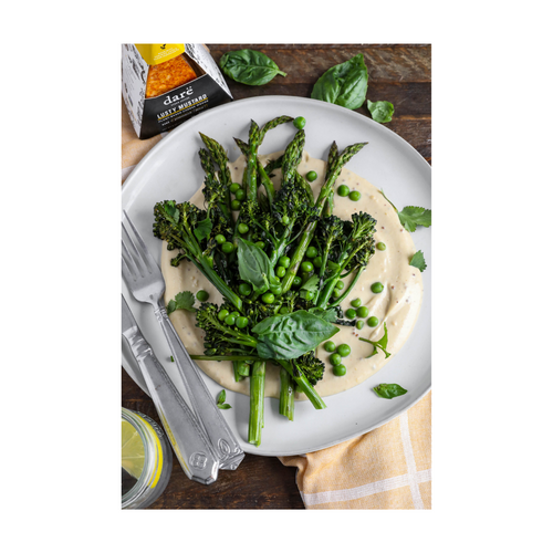 Load image 1 in gallery view. Green vegetables over a bed of vegan lusty mustard cheese sauce on a white plate with a silver fork and knife on the side.