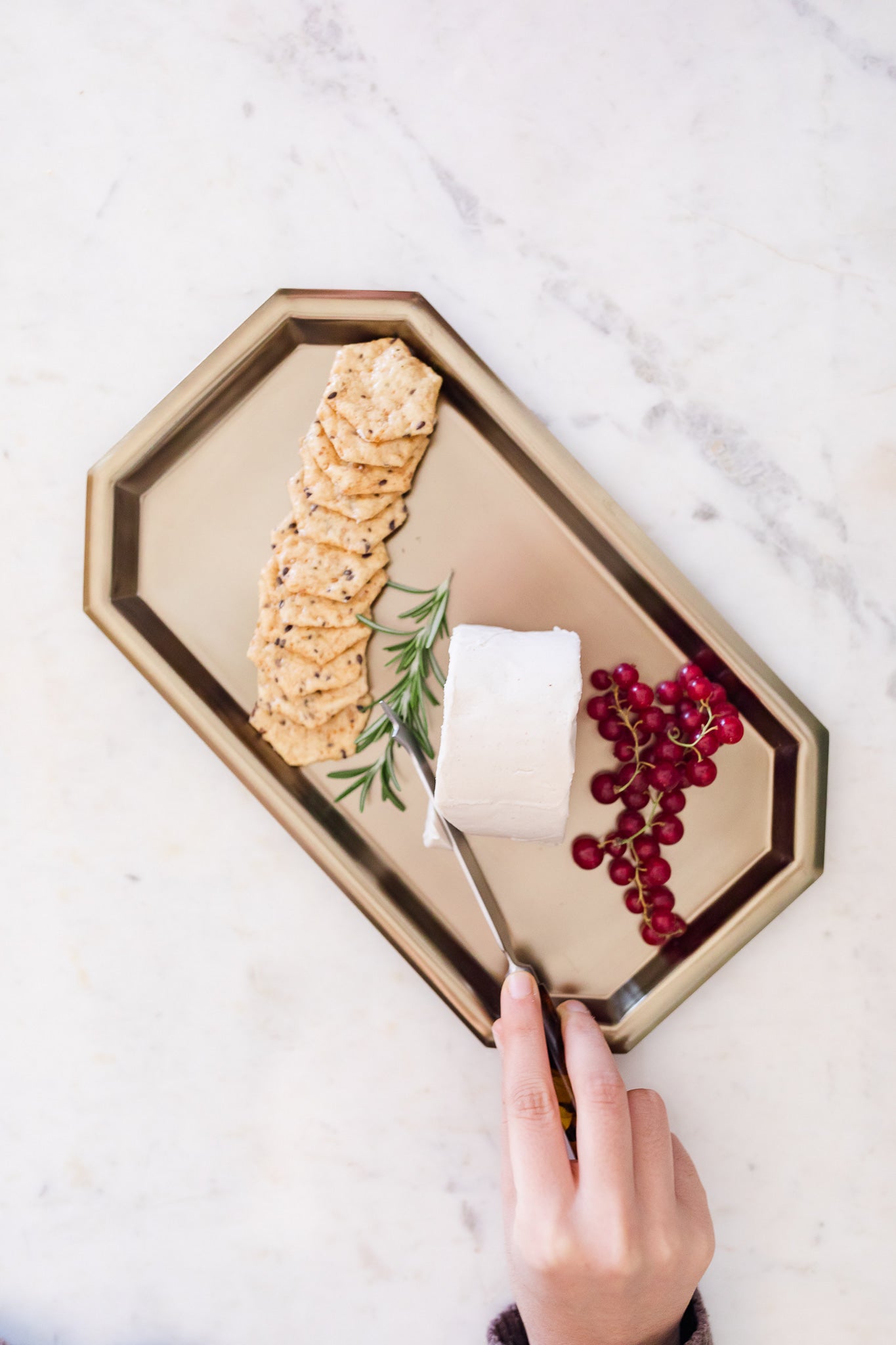 Gold tray with Oh My Goat cheese, crackers, and red berries on a marble surface