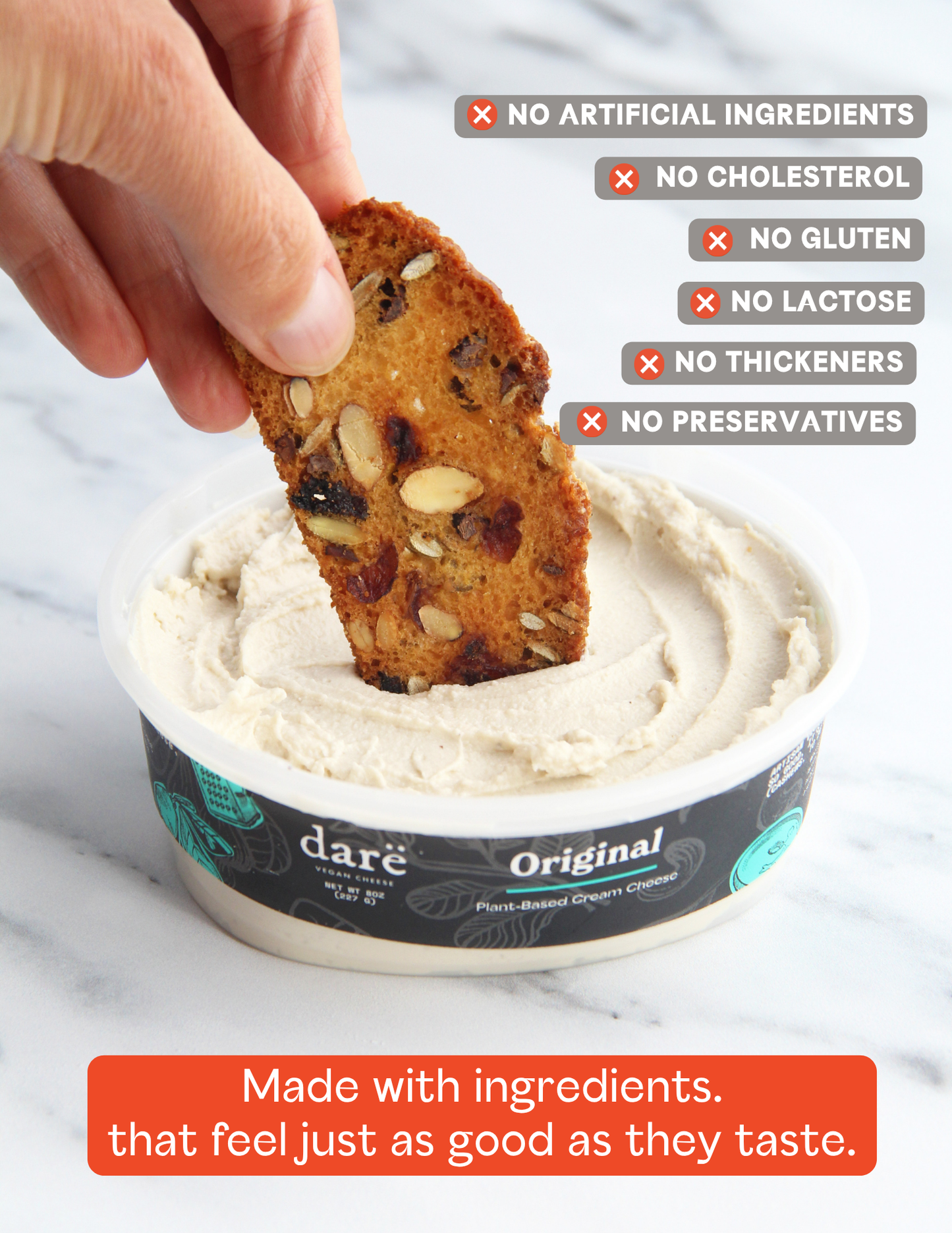 A hand dipping a seeded cracker into a tub of dare vegan cheese Original plant-based cream cheese on a white marble surface, with text callouts about ingredients.