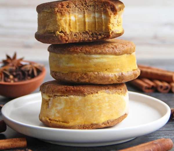 Three stacked pumpkin spice ice cream sandwiches on a white plate, with cinnamon sticks and star anise in the background.