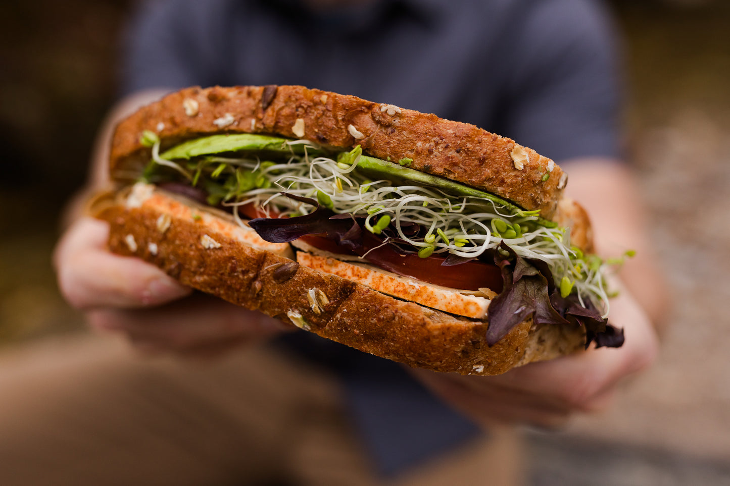 Hand holding a sandwich with visible ingredients against a blurred background