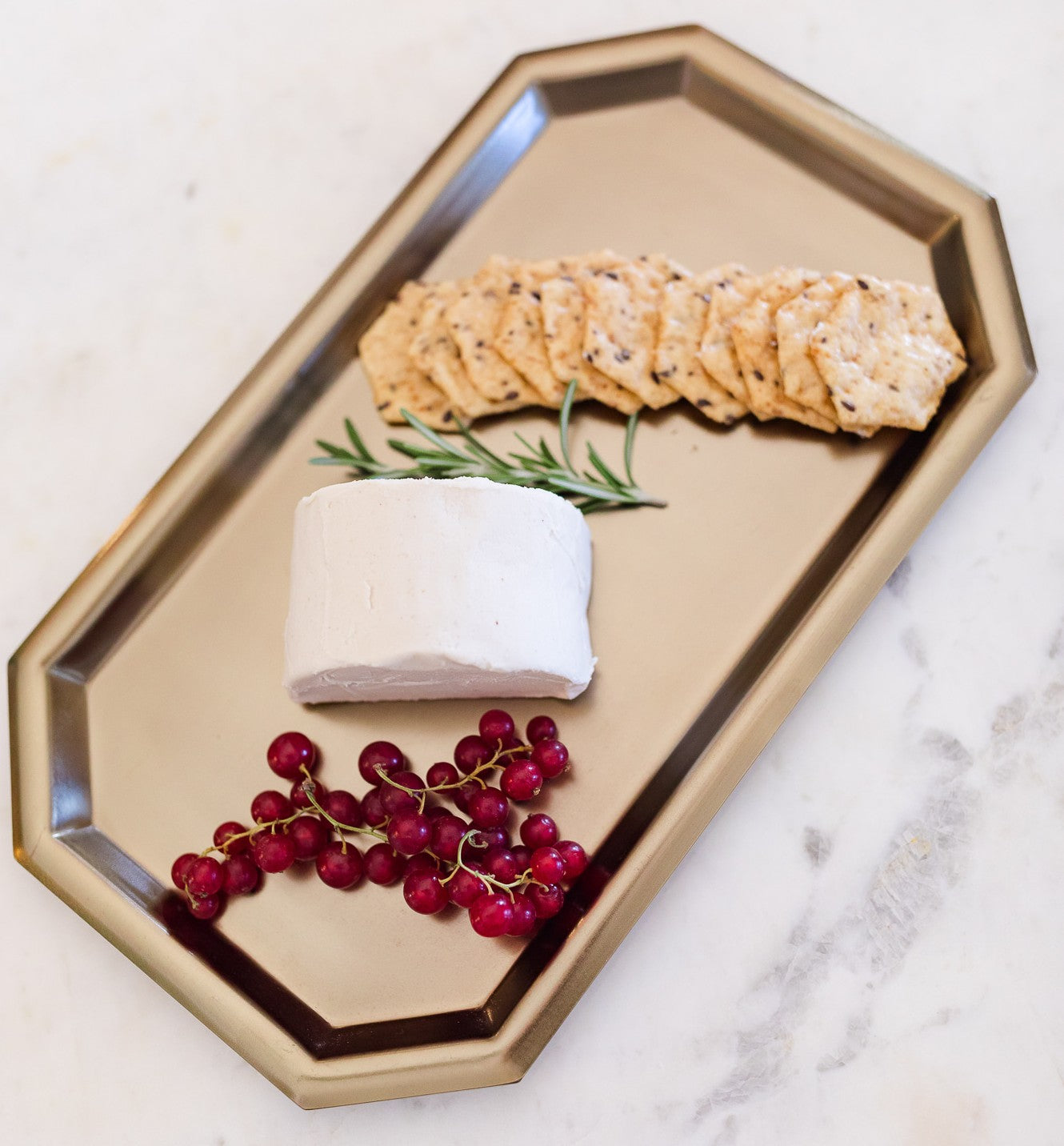 Block of vegan goat cheese with crackers and red berries on a gold hexagonal tray.