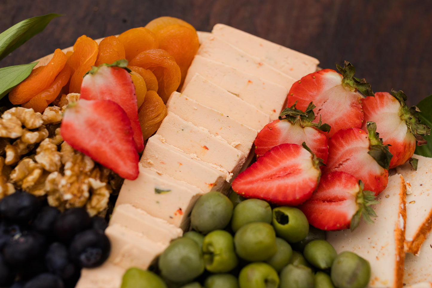 Platter of cheese, fruit, and nuts on a wooden surface