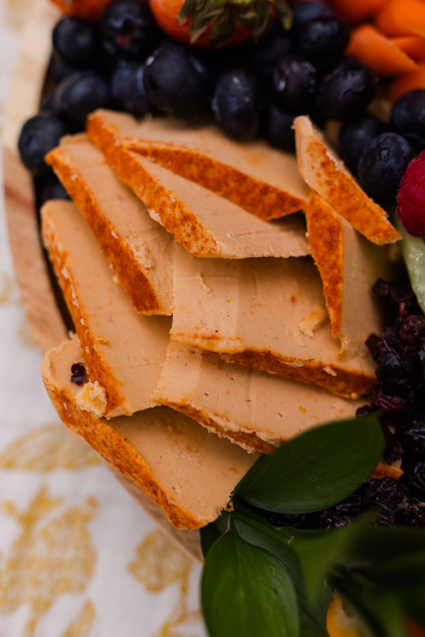 Platter of sliced plant based smoked cheddar cheese with fruits and vegetables on a decorative plate