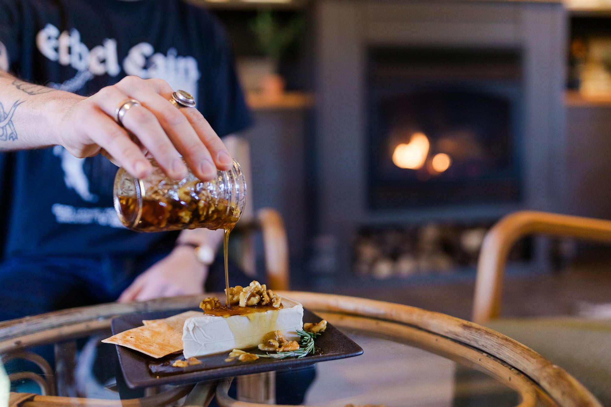 Maple syrup poured onto Darë Vegan Cheese Roasted Garlic Cheese Wedge with a fireplace in the background