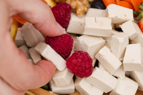Load image 1 in gallery view. Close-up of a hand picking up a raspberry from a plate of assorted fruits and cheese.