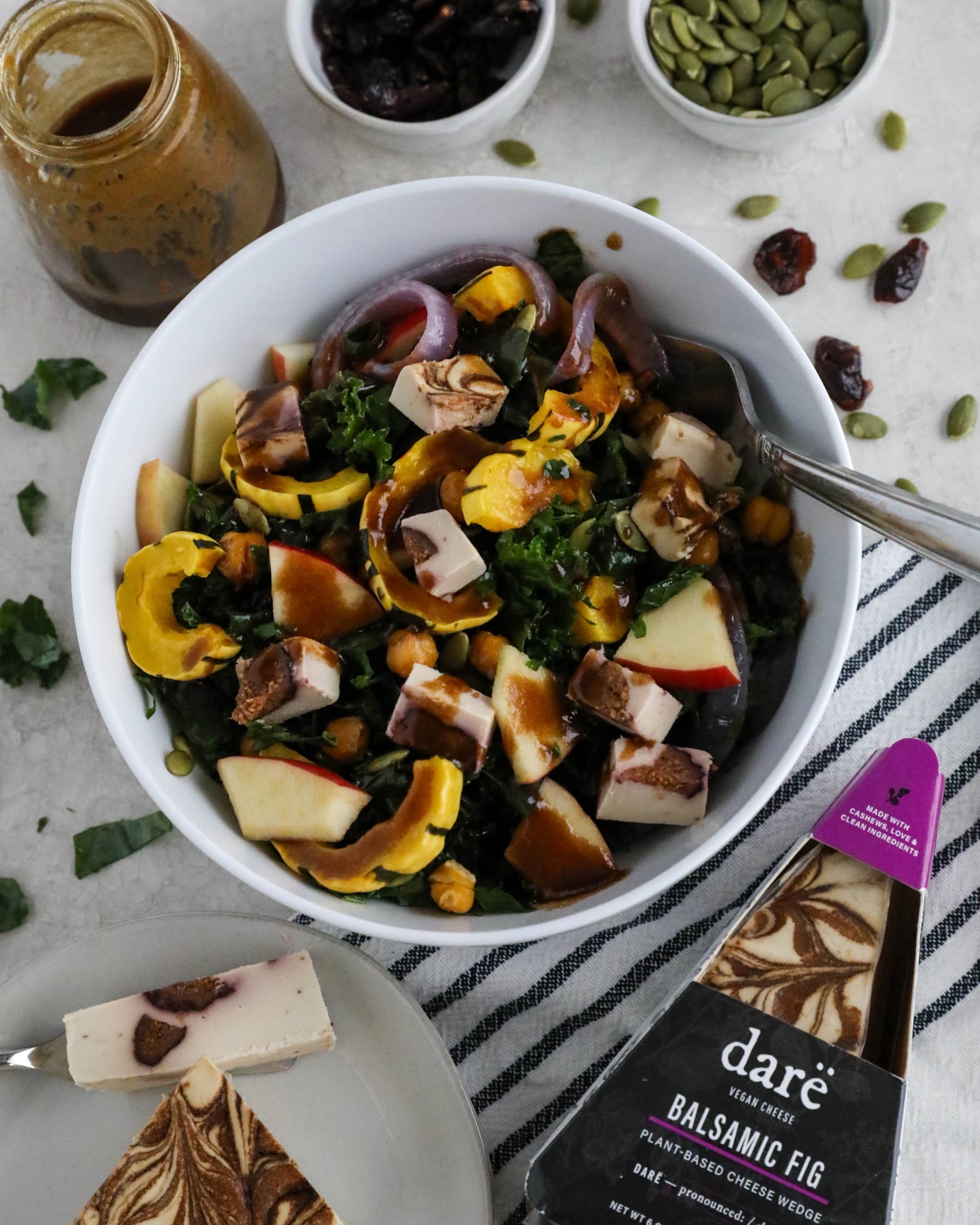 Salad with various ingredients in a white bowl on a table with a bottle of balsamic fig dressing.
