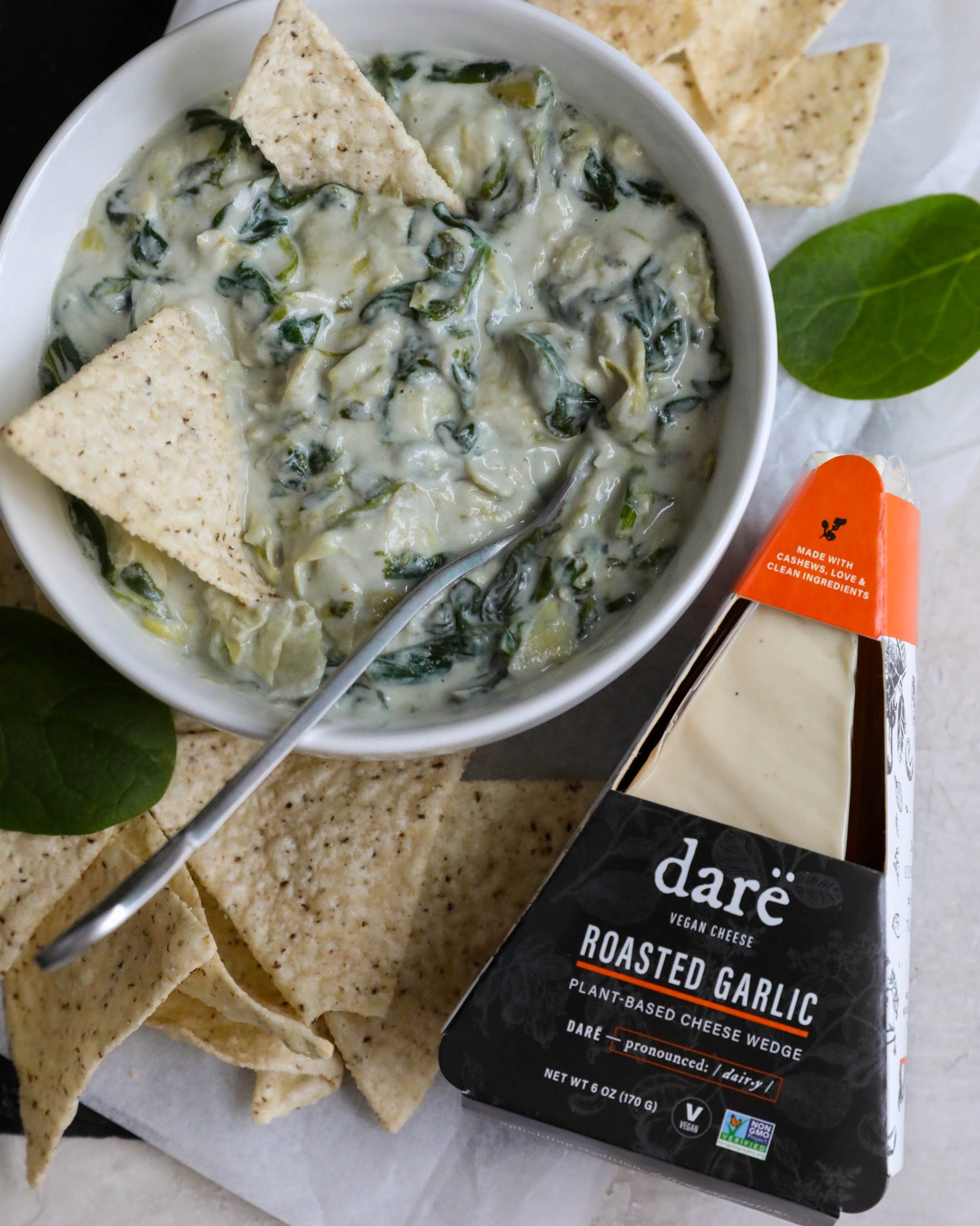 Bowl of spinach artichoke dip with tortilla chips and a package of dare roasted garlic cheese.