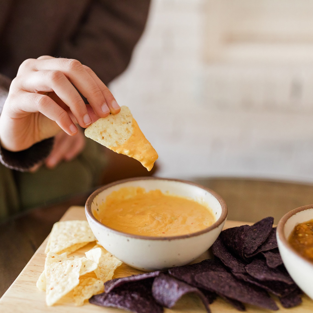 Hand holding tortilla chip dips into Darë Vegan Cheese Spicy Queso