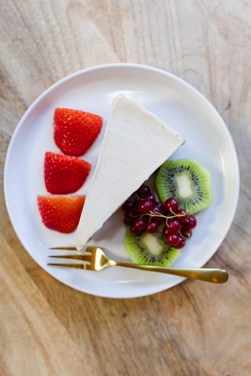 Load image 1 in gallery view. Darë Vegan Cheese Original Cheesecake on a plate with fruit. white plate sitting on wooden counter. cheesecake surrounded by fresh fruit slices and gold fork