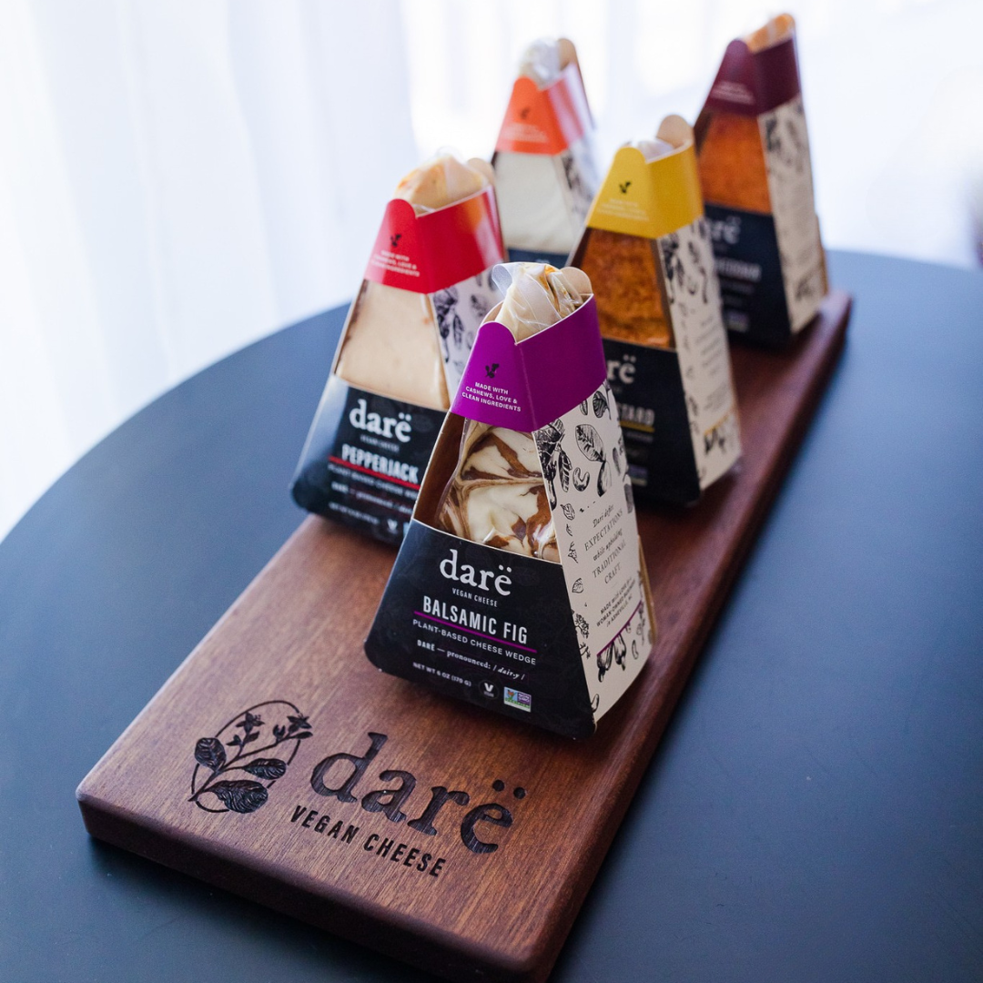 Darë Vegan Cheese brand dairy free cheese wedges on a wooden cheese board. all in black and colored packaging.
