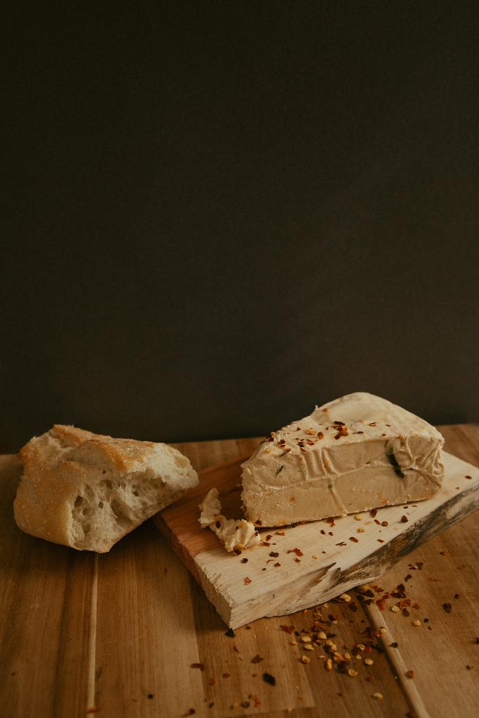 pepper jack cheese on wooden cutting board. piece of bread next to cheese. cheese sprinkled with red pepper flakes