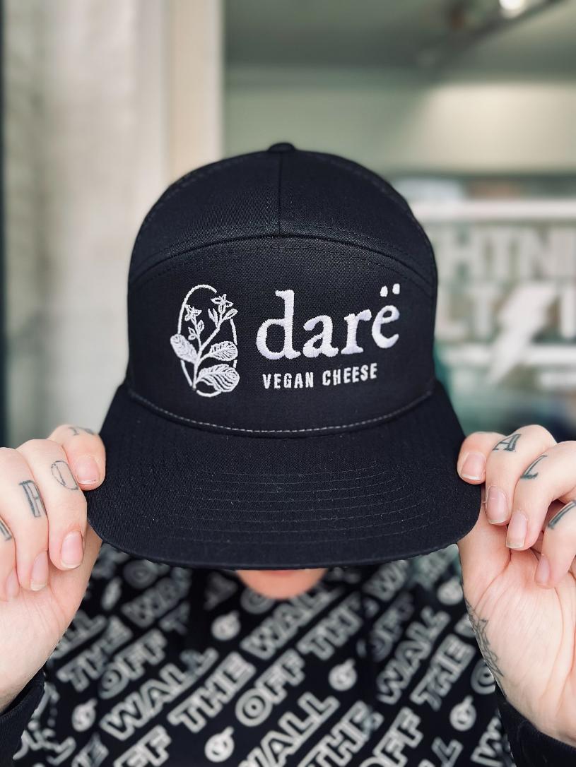 black and white dare trucker hat that reads dare vegan cheese. white flower logo on front side