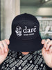 black and white dare trucker hat that reads dare vegan cheese. white flower logo on front side