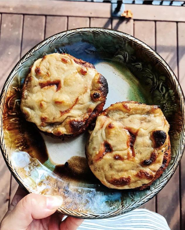 pizza bagel on beautiful green pottery plate. held by a hand, two halves of a bagel topped with vegan gouda and tomato sauce